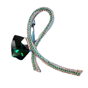 Elegant crystal bow brooch with a large green gemstone and shimmering pavé ribbon
