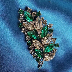Macro shot of silver leaf brooch with green marquise stones and crystals on blue silk