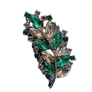Elegant gold leaf brooch with emerald and champagne crystals on a clean white background