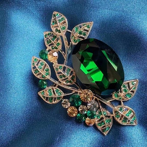 Macro detail of emerald crystal brooch with golden leaf design and green gemstones