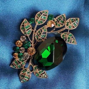 Detailed macro view of vintage emerald leaf brooch with green crystals on blue silk fabric