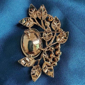 Elegant gold emerald leaf brooch with crystals and safety pin on blue silk background