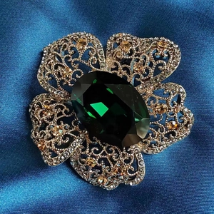 Macro view of a vintage floral brooch with emerald green gemstone and gold openwork petals