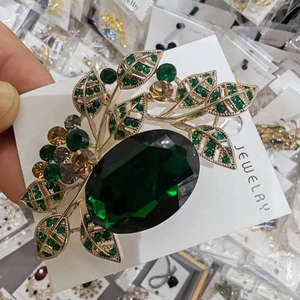 Detailed macro of the emerald green leaf brooch with crystal-studded golden finish