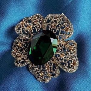 Macro shot of vintage emerald crystal flower brooch with gold plating on blue silk