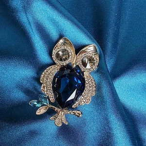 Exquise broche hibou dorée avec cristal goutte bleu foncé sur tissu en soie bleue