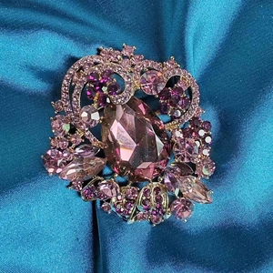 Luxurious vintage gold brooch with teardrop purple crystal on blue silk background