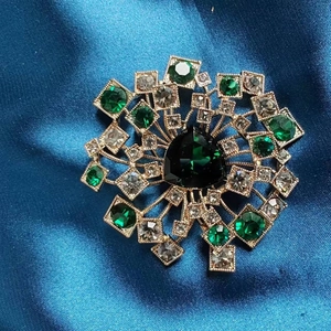 Macro di una spilla a dente di leone con cristalli verde smeraldo su raso blu