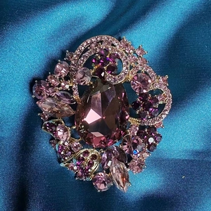 Macro detail of luxury purple crystal brooch featuring pear-shaped stone on gold alloy