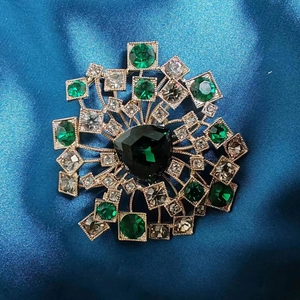 Dettaglio della spilla a dente di leone in cristallo smeraldo su seta blu