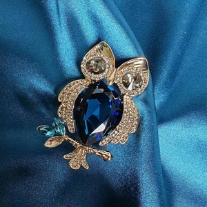 Détail macro d'une broche hibou dorée avec cristal bleu nuit sur tissu en soie