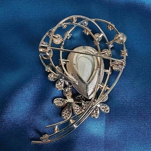 Verso de l'élégante broche fleur argentée avec cristaux sur fond de soie bleue satinée