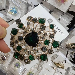 Dettaglio della spilla a cuore smeraldo con montatura dorata e cristalli stile dente di leone