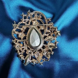 Vintage golden crystal brooch with teardrop stone and pin back on blue satin