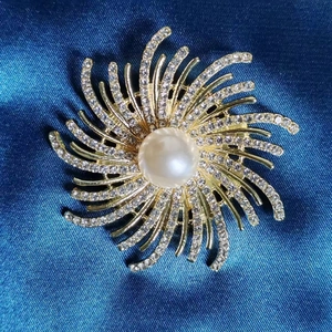 Détail macro d'une broche fleur avec perle centrale et cristaux sur fond bleu