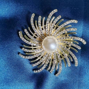 Détail macro d'une broche fleur dorée vintage avec perle centrale et strass brillants