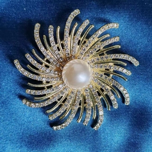 Broche fleur dorée élégante avec perle et strass sur fond de satin bleu foncé soyeux