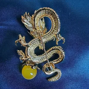 Elegant gold dragon brooch with yellow bead detail on dark blue silk background