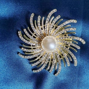 Élégante broche soleil dorée avec perle centrale et strass blancs scintillants