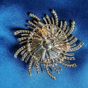 Vue arrière d'une broche fleur plaquée or avec épingle de sûreté sur tissu en soie bleue