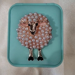Charming golden sheep brooch with inlaid white pearls on a light mint gift box