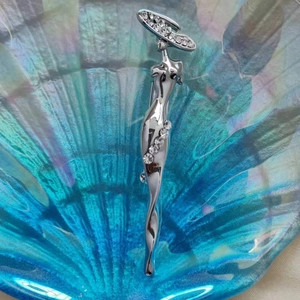 Détail d'une élégante broche argentée représentant une femme au chapeau sertie de strass