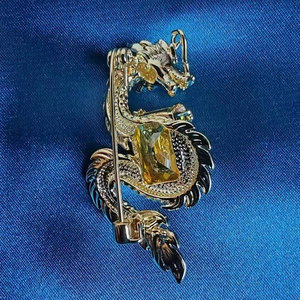 Detailed close-up of golden dragon brooch with yellow gemstone and zircon inlays