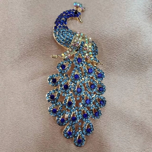 Elegant gold-tone peacock brooch inlaid with vibrant blue rhinestones on beige fabric