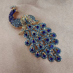 Close-up of golden peacock brooch with sparkling blue rhinestones on silk fabric