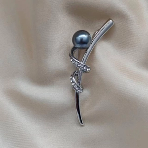 Detail einer eleganten silbernen Bandschleife-Brosche mit dunkelgrauer Perle und kleinen Steinen
