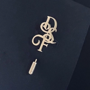 Elegant silver script letter lapel pin on dark blue suit fabric for formal business wear