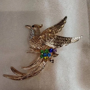 Spilla uccello fenice dorata con cristalli multicolore su sfondo di seta elegante