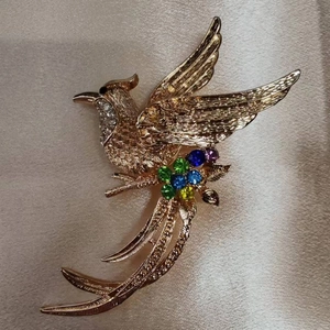 Vista dettagliata della spilla a fenice dorata con strass colorati su sfondo di raso