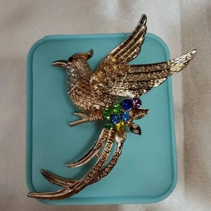 Dettaglio di una spilla a fenice dorata con cristalli colorati e trama fine delle piume