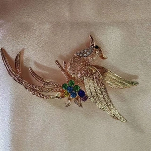 Dettaglio di una spilla a fenice con strass multicolore su sfondo in seta