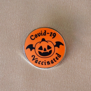 Detail of Jack-o'-lantern enamel pin with bat wings and Covid-19 Vaccinated text