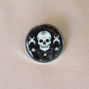 Close-up of a Gothic enamel brooch featuring a skull, spiderweb, and moon symbols