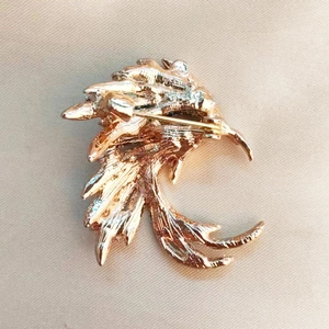 Rose gold feather brooch with secure safety pin clasp on premium beige silk background