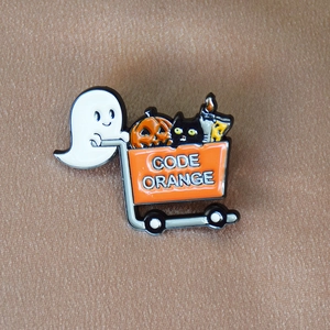Detail of Halloween enamel pin showing ghost with pumpkin cart and black cat on fabric