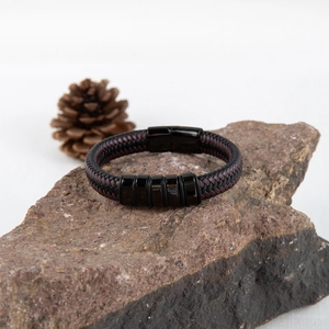 Détail du bracelet en cuir tressé sur roche avec fermoir magnétique et anneaux noirs