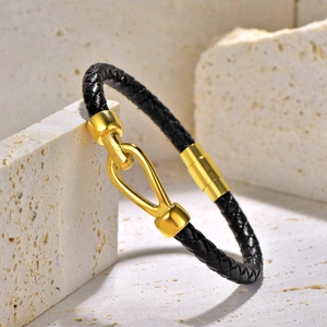 Close-up of black braided leather bracelet with golden horseshoe buckle on stone