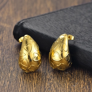 Détail de boucles d'oreilles gouttes dorées avec motifs de cœurs sur acier inoxydable