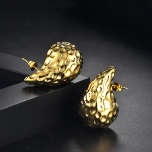 Détail des boucles d'oreilles goutte dorées 18K avec texture martelée sur support noir