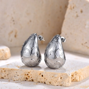 Gros plan de boucles d'oreilles gouttes argentées avec texture cœur sur pierre