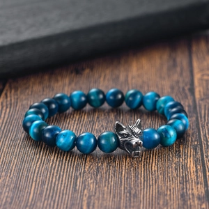 Macro shot of blue tiger eye beads and an intricate silver wolf head charm on a wooden table
