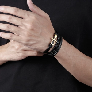 Détail d'un bracelet multicouche en cuir noir avec un charm croix Ankh dorée