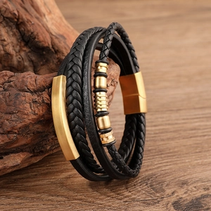 Detail of multi-layer black braided leather bracelet with golden magnetic clasp on wood