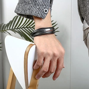 Detalle de una pulsera multicapa de cuero negro para hombre con placa de acero inoxidable