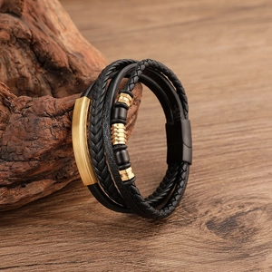 Detail of multi-layer black braided leather bracelet with matte gold metal accents