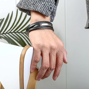 Detalle de una pulsera de cuero negro trenzado multicapa con placas de metal plateado en muñeca